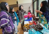 Women stop at a table where another women talks about her culture.