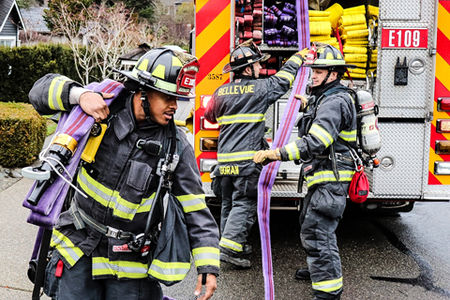 Three fire fighters in a gear removing a hose from a fire truck