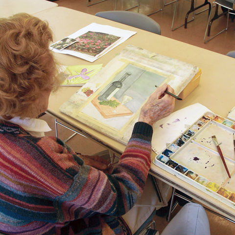 elderly woman painting in a notepad