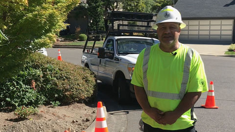 A city worker stands in front of a street maintenance truck on a side street