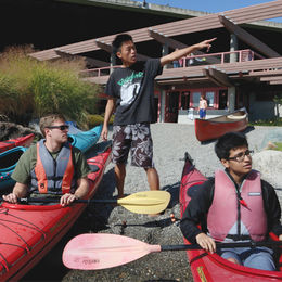 Two guys in kayaks and a guide pointing something in distance