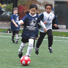 A girl with a red soccer ball being chased by two other children on a field