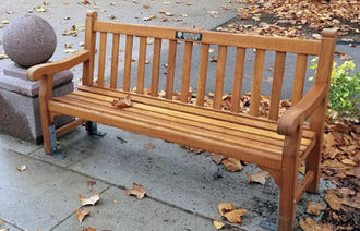 wooden park bench on a concrete path with a granite ball on a stand next to it