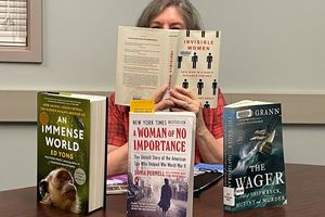 image of person at table holding up book. Three more books are placed on table.